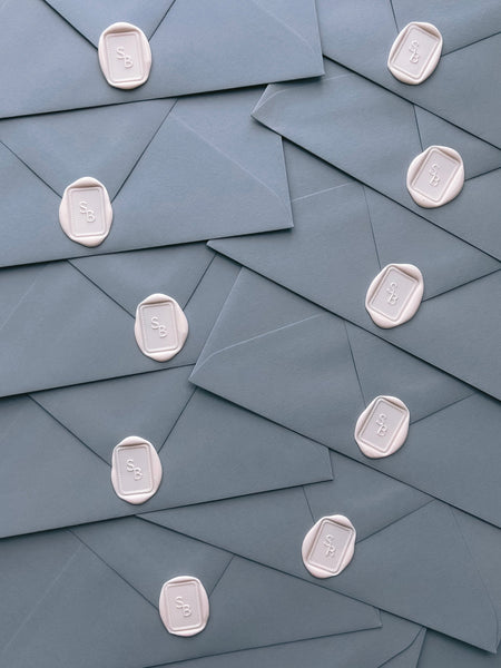 Rectangular dotted border monogram wax seals in ivory nude on dusty blue envelopes