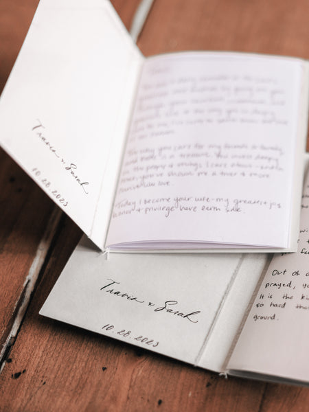 Personalized names and wedding date in calligraphy on the inner cover of a set of beige vow books with handwritten vows