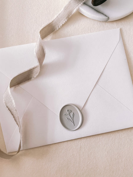 Simple flower oval wax seal in dove gray on a white paper envelope styled with a strand of taupe colored silk ribbon