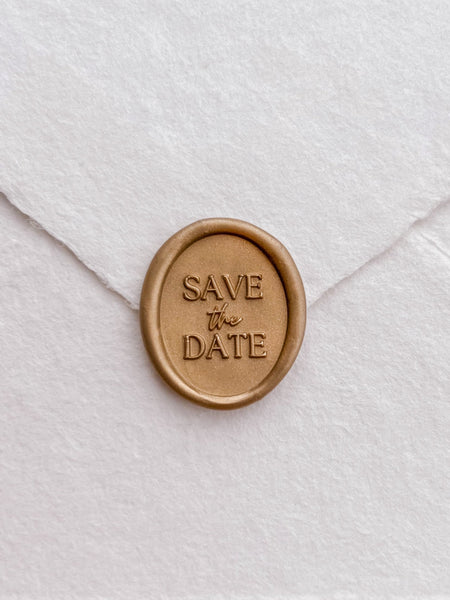 Gold Save The Date oval wax seal on a white envelope