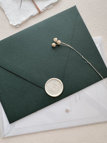 off-white botanical wax seal featuring a leaf branch design on a dark green envelope