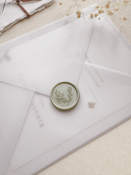 light metallic sage green wax seal featuring a delicate leaf design on a vellum wedding invitation envelope