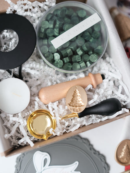 Christmas wax stamp kit with Christmas tree wax stamp, metallic green sealing wax beads, and melting tools such as a metal stove, candle and spoon