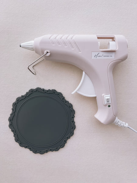 beige low heat glue gun for wax seal making, next to a gray silicone mat