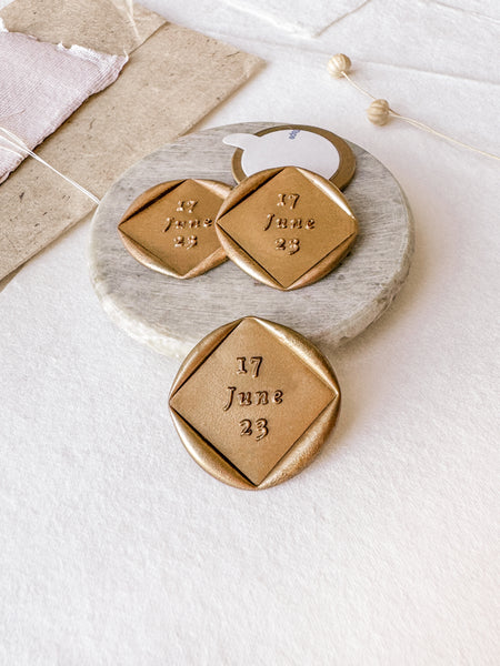 Personalized wedding date diamond custom wax seals in gold styled with a small gray stone dish, handmade paper and a dried floral branch