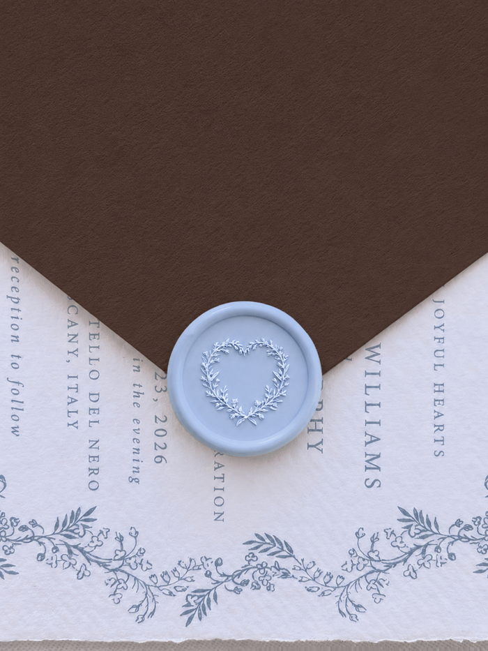 light blue heart shaped botanical wreath wax seal on a dark brown envelope flat and a blue botanical themed wedding invitation card