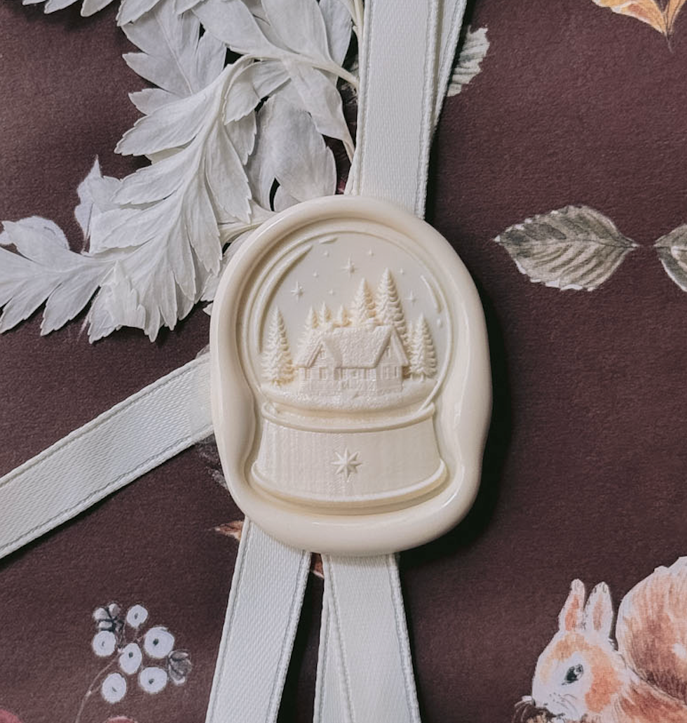 Off-white snow globe wax seal on a wrapped Christmas gift