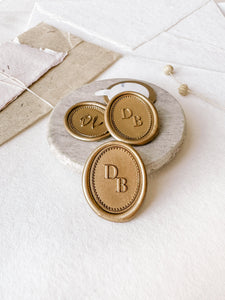 Oval monogram gold wax seals on a gray stone dish