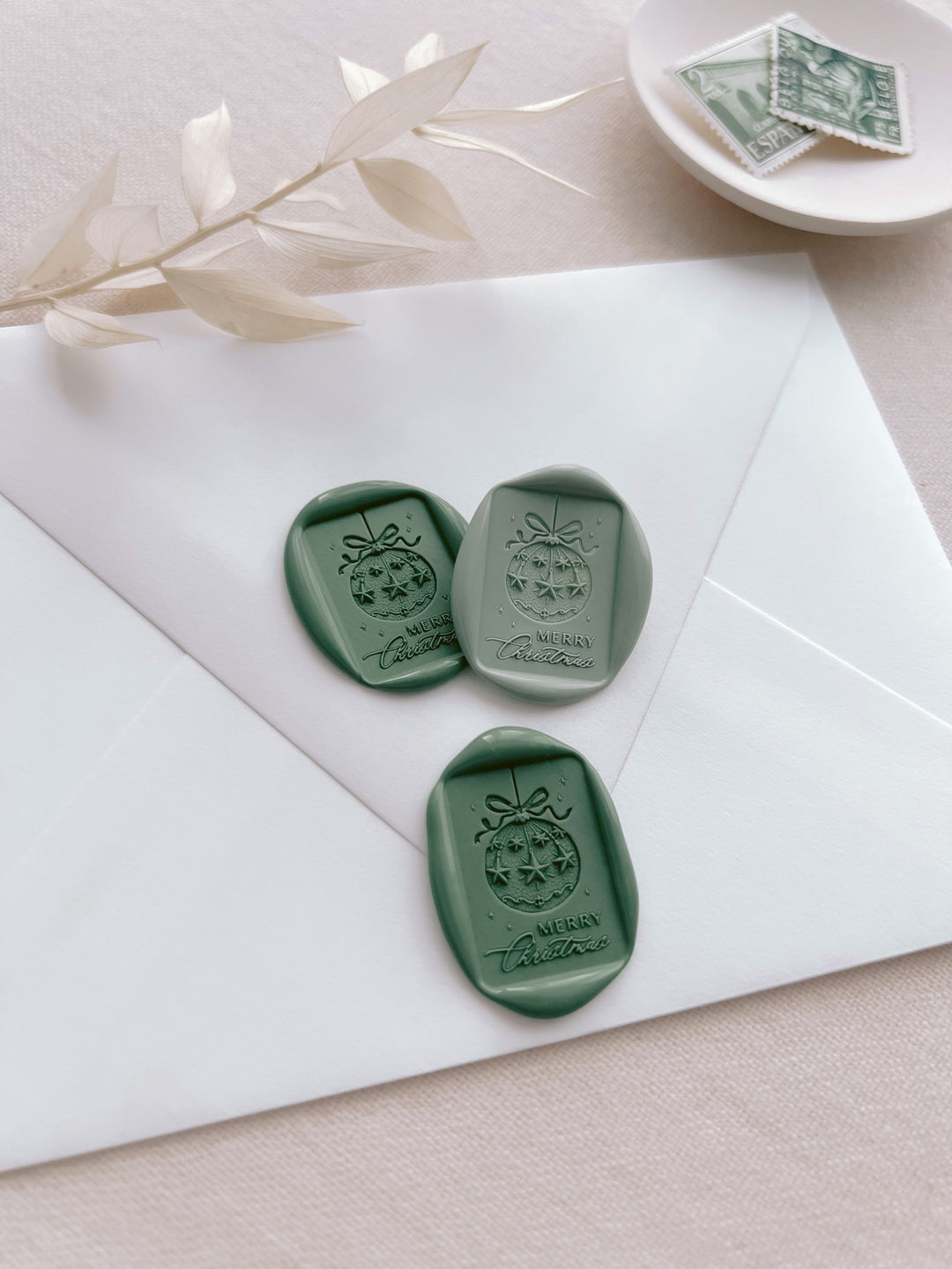 three green Christmas ornament Merry Christmas wax seals placed on a white envelope