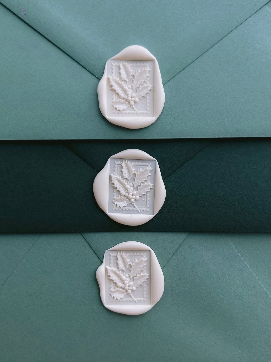 three white wax seals with festive holly leaf design on green Christmas card envelopes