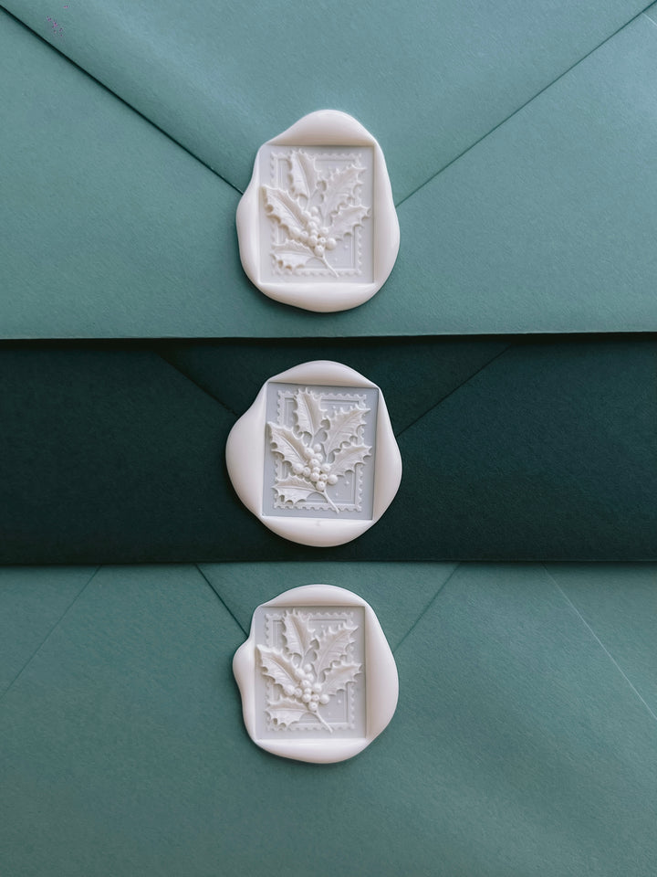 three white wax seals with festive holly leaf design on green Christmas card envelopes