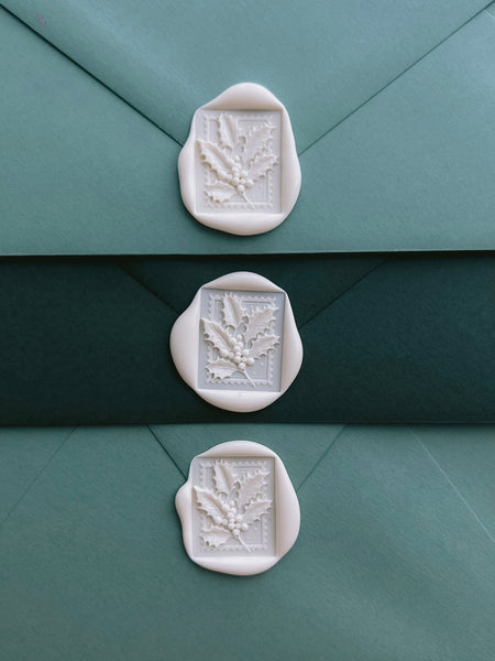 three white wax seals with festive holly leaf design on green Christmas card envelopes