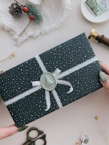 Pearlescent light green 3D Christmas tree oval wax seal placed on a wrapped gift box with white silk ribbon