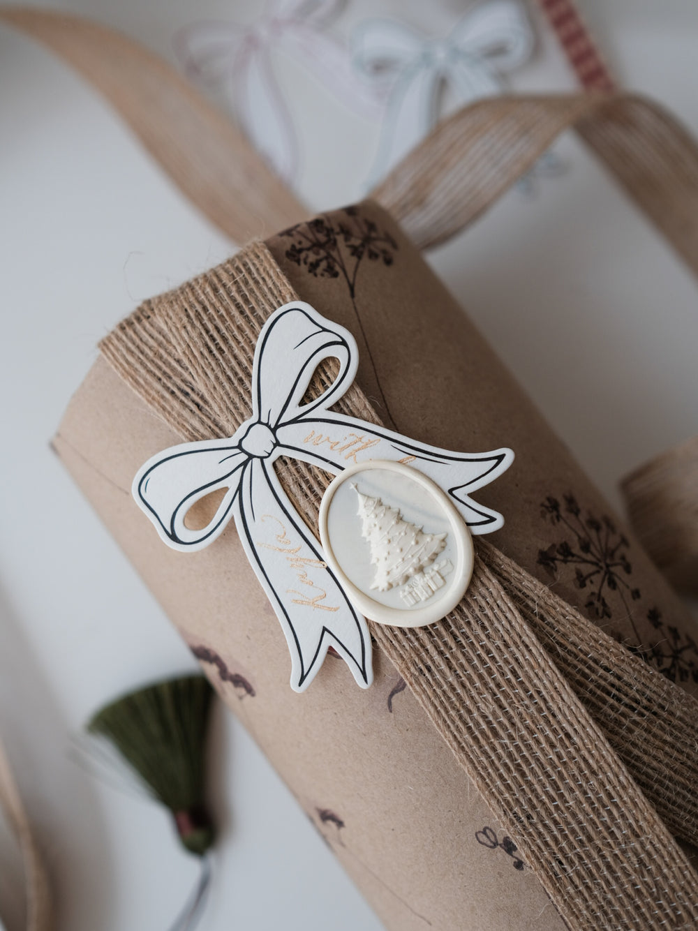 Antique white oval 3D-engraved Christmas tree wax seal on a personalized die-cut ribbon shaped gift tag on a wrapped Christmas gift 