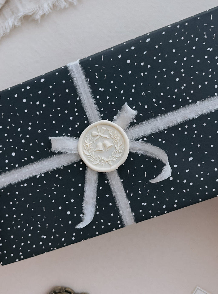 Off-white festive Christmas wreath with jingle bells wax seal on a wrapped Christmas gift