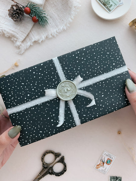 Metallic light green Christmas wreath and jingle bells wax seal on a wrapped holiday gift