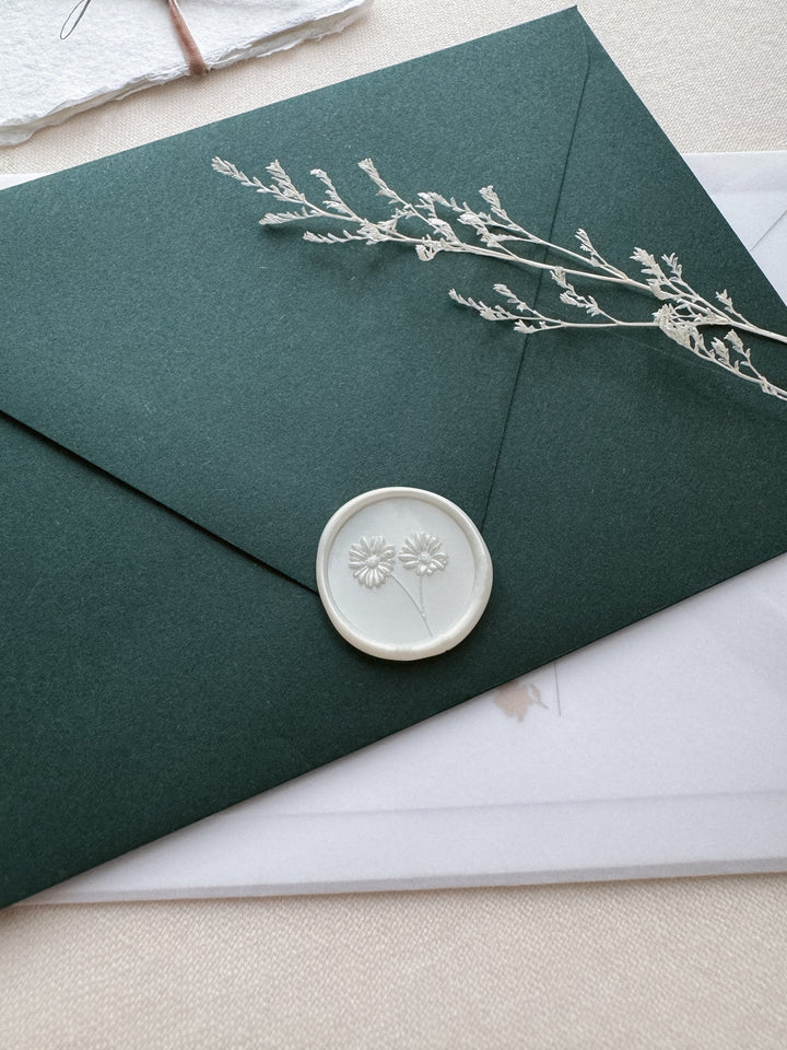 pearl white daisy wax seal on a dark green envelope