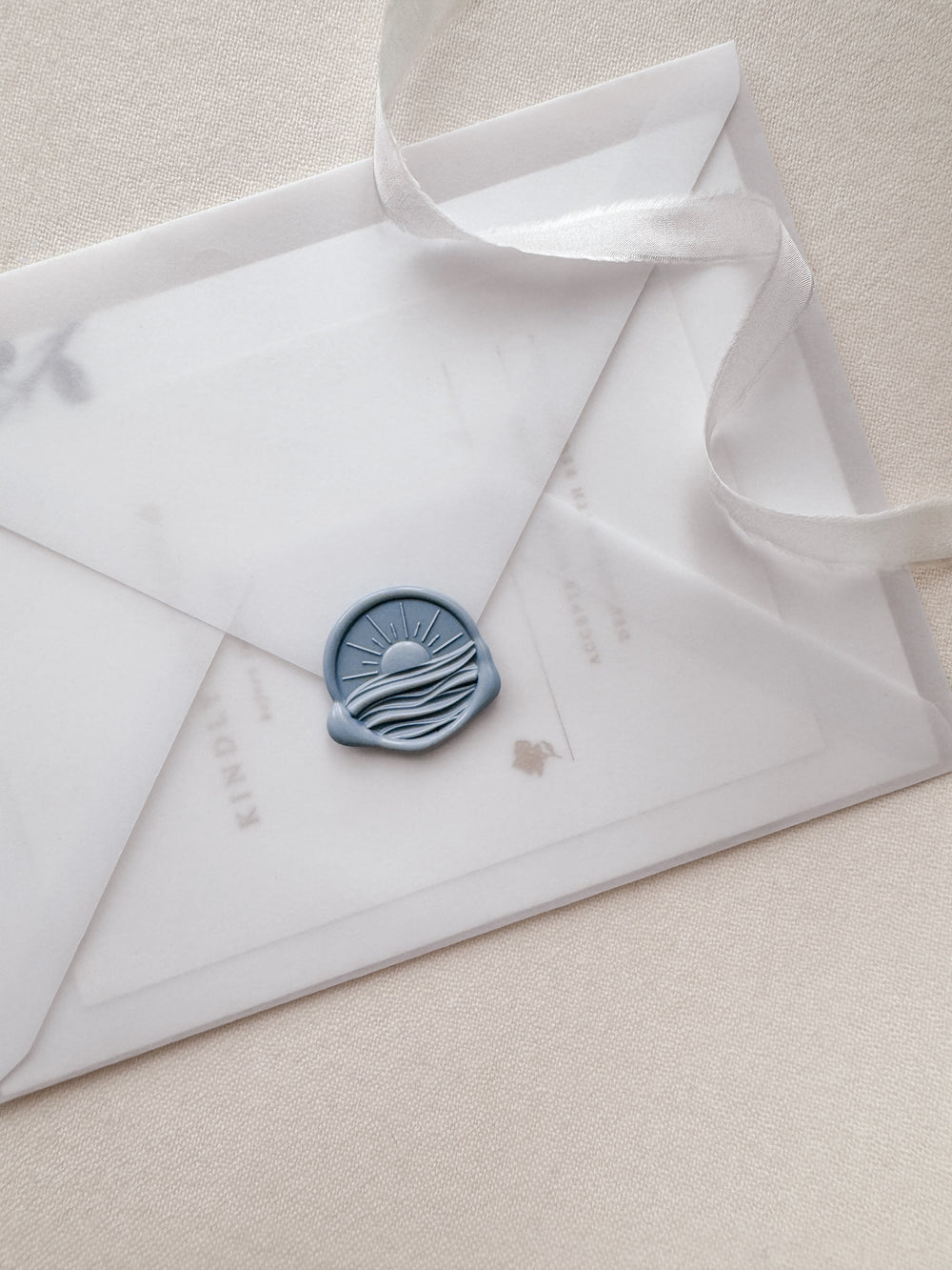Dusty blue 3D sunset and ocean wax seal on a vellum wedding invitation envelope