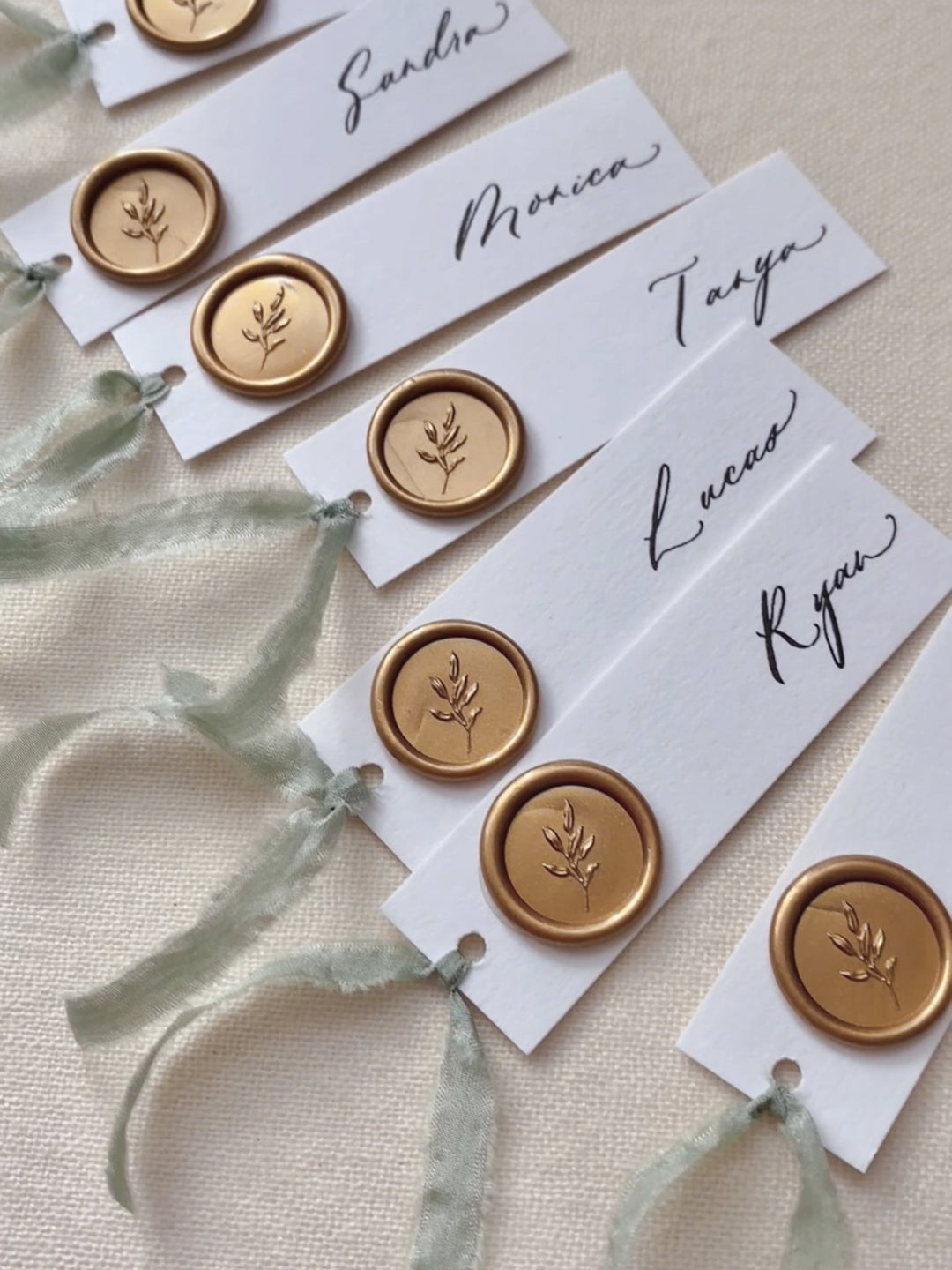 Gold mini leaf wax seals on white wedding place cards tied with sage green silk ribbon 