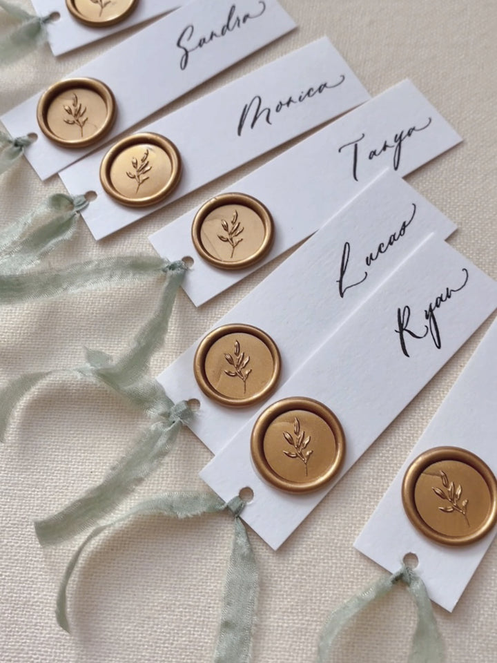 Gold mini leaf wax seals on white wedding place cards tied with sage green silk ribbon 