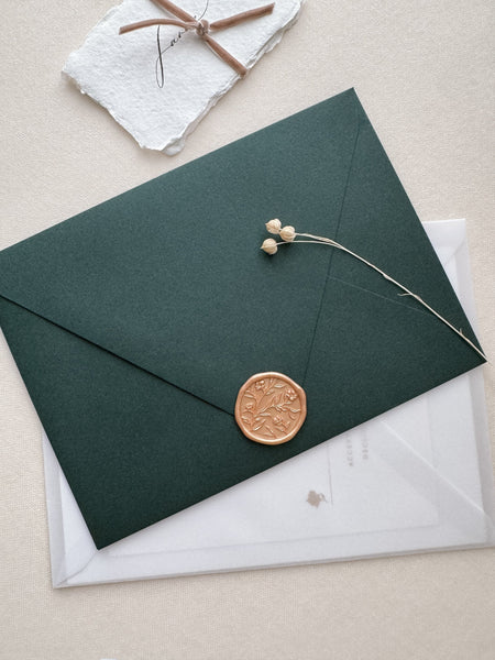 Peachy gold colored floral pattern wax seal with 3D engraving on a dark green envelope