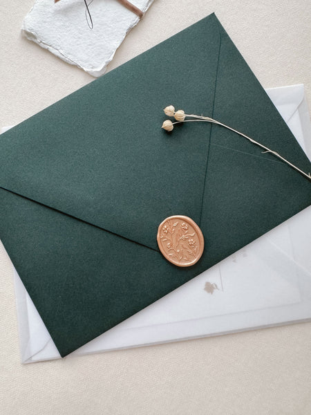 Peachy gold colored floral pattern oval wax seal with 3D engraving details on a dark green envelope