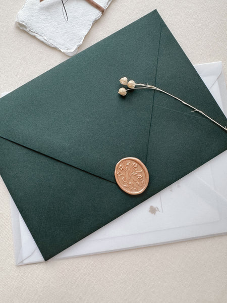Peachy gold colored oval floral pattern wax seal with 3D engraving on a dark green envelope