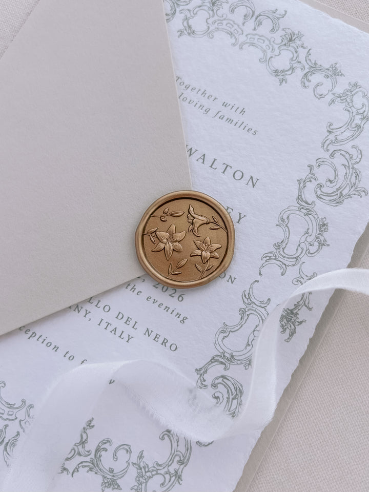 gold 3D lilies floral wax seal on a beige envelope over a white deckle-edge wedding invitation card