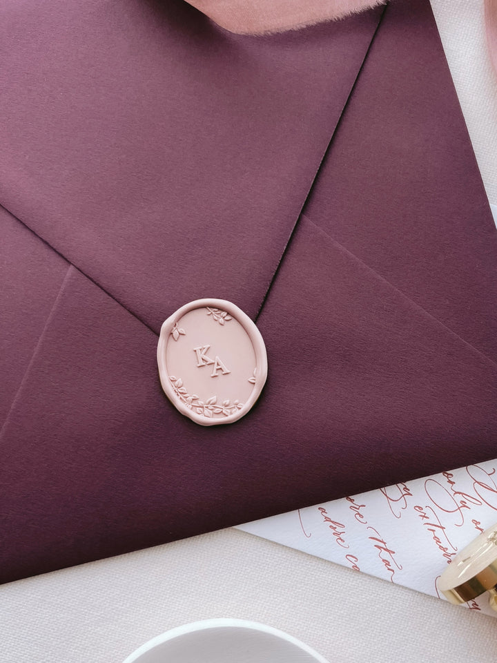 Light pink oval monogram wax seal with personalized initials and 3D engraved botanical leaves and branches on a burgundy envelope 