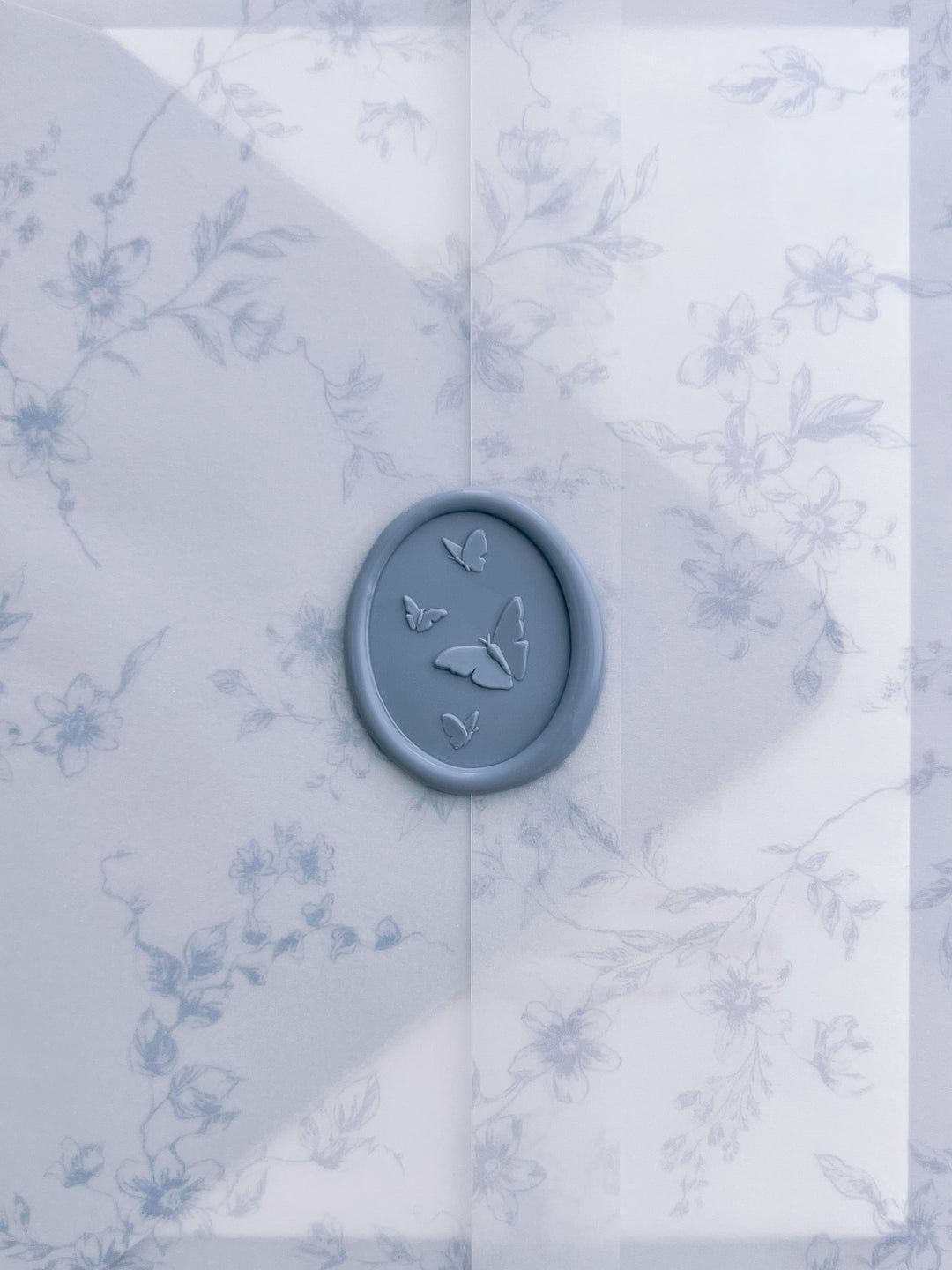 light blue 3D butterflies oval wax seal on a floral vellum wrap with blue botanical pattern