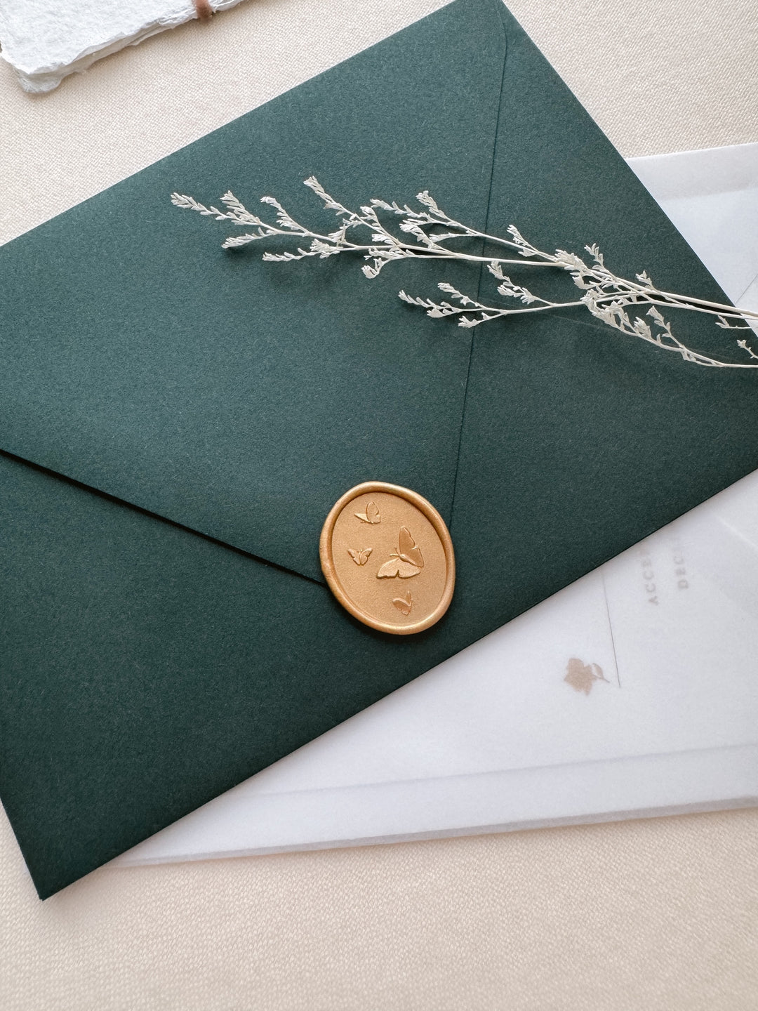 gold 3D butterflies wax seal on a dark green wedding paper envelope on a cream textured background
