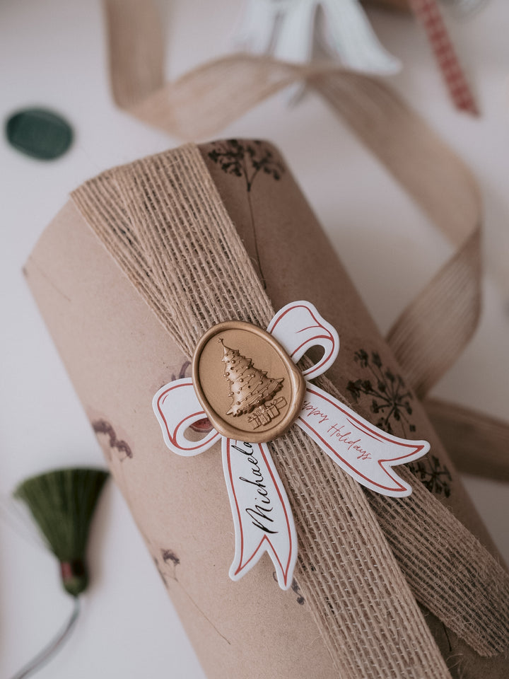 Gold 3D Christmas tree oval wax seal on a personalized die-cut ribbon shaped gift tag on a wrapped Christmas gift