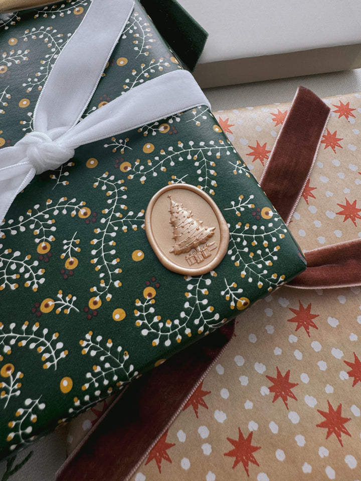 Matte light gold 3D Christmas tree oval wax seal on a Christmas gift wrapped in festive botanical wrapping paper 