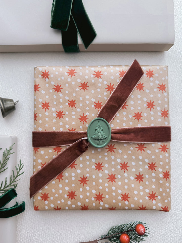 Sage green 3D-engraved Christmas tree oval wax seal on a brown ribbon tied on a gift wrapped in festive gift wrapping paper