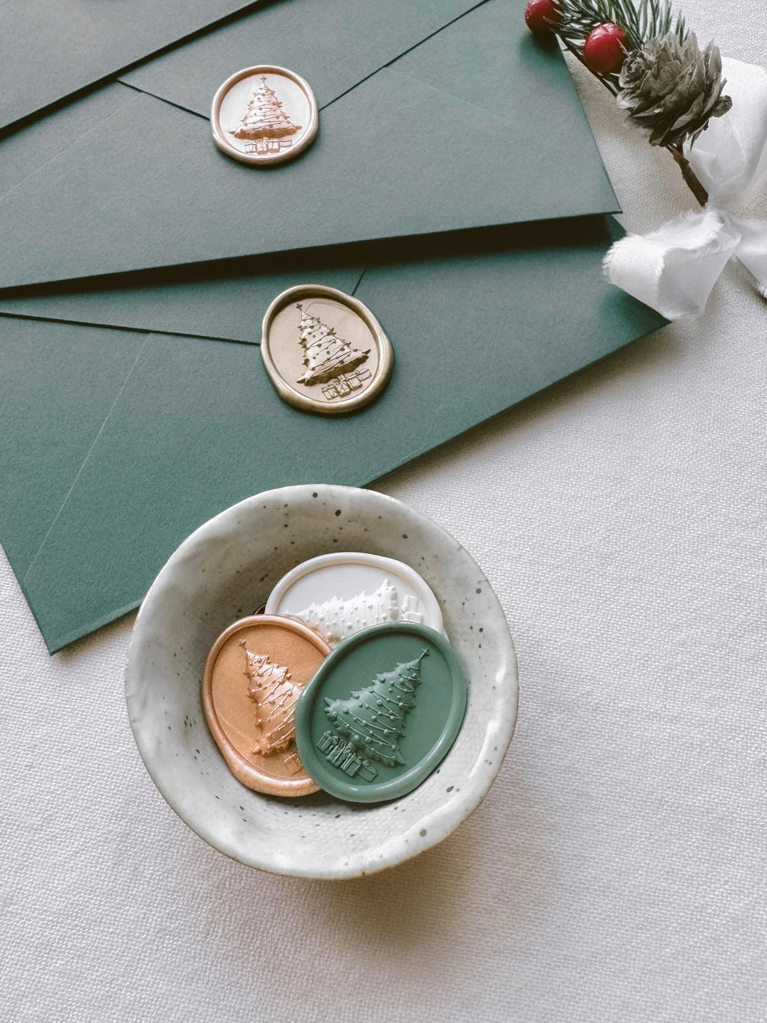Sage green, peachy gold, and antique white 3D Christmas tree oval wax seals in a ceramic dish and on dark green envelopes