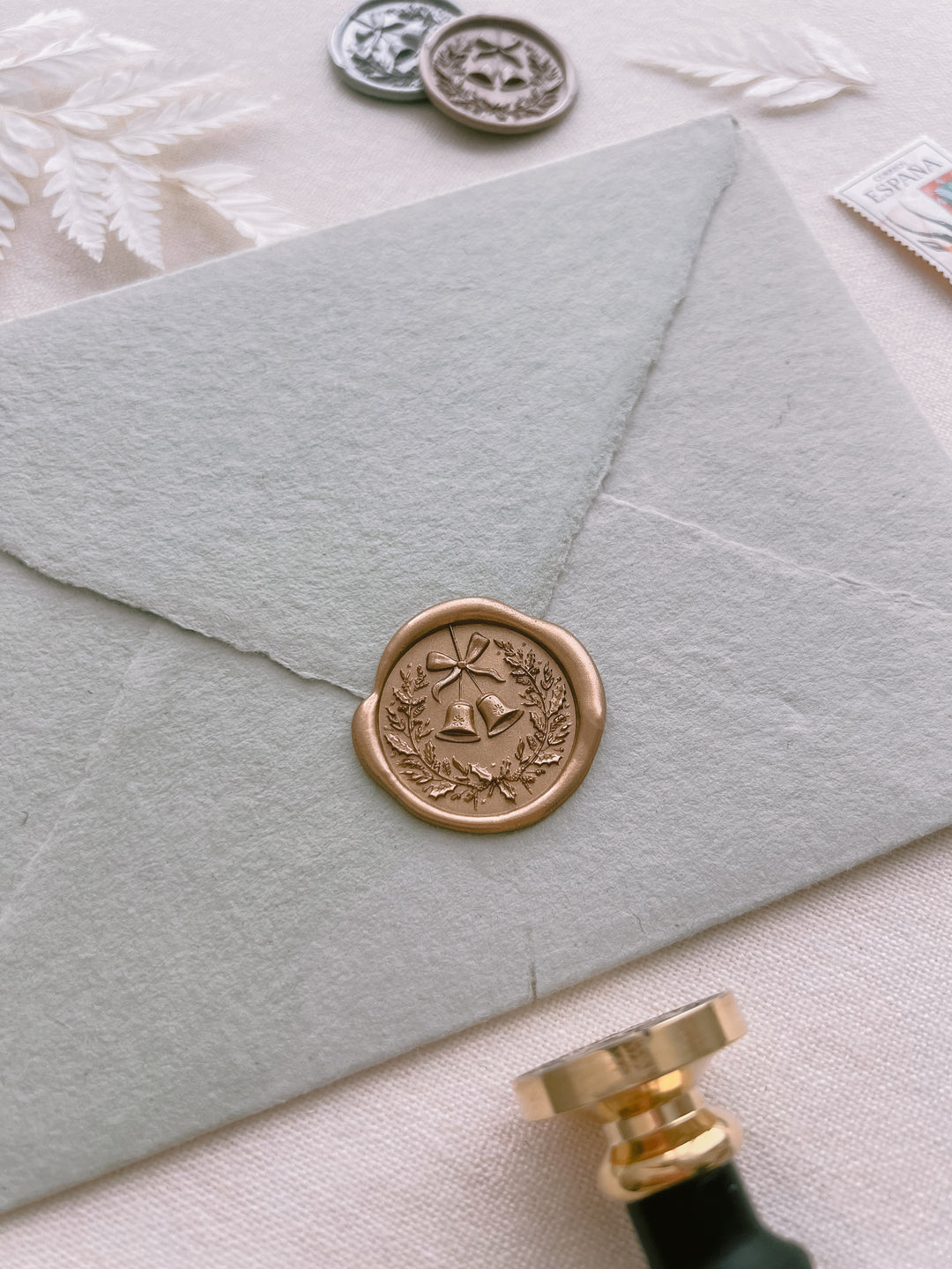 Christmas wreath jingle bells gold wax seal on a light sage green envelope 