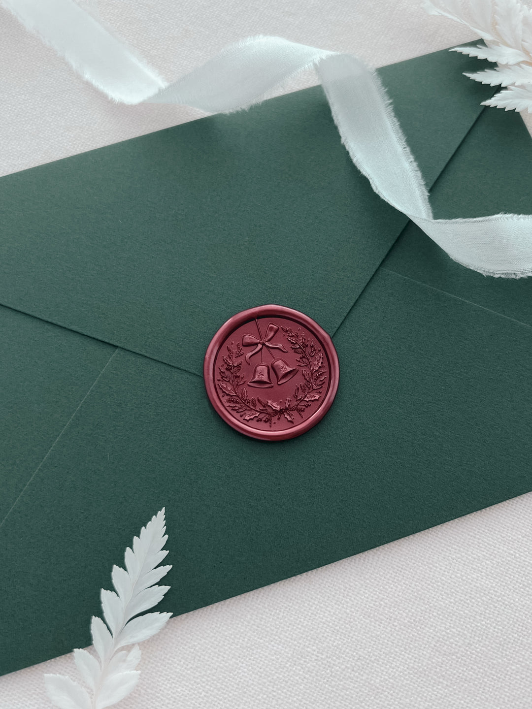 Dark metallic red 3D Christmas wreath and jingle bells wax seal on a dark green envelope