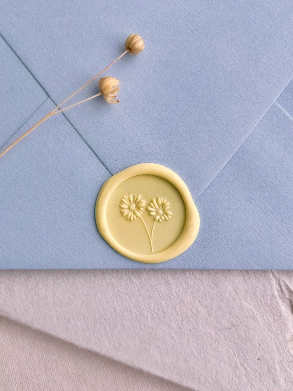 Soft yellow daisy wax seal on a pale blue wedding invitation envelope