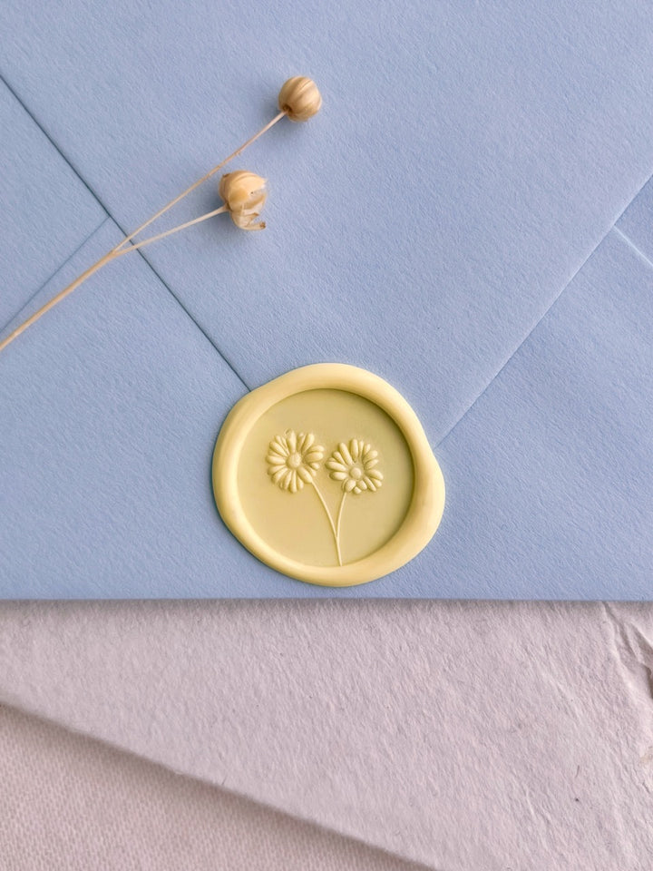 Soft yellow daisy wax seal on a pale blue wedding invitation envelope