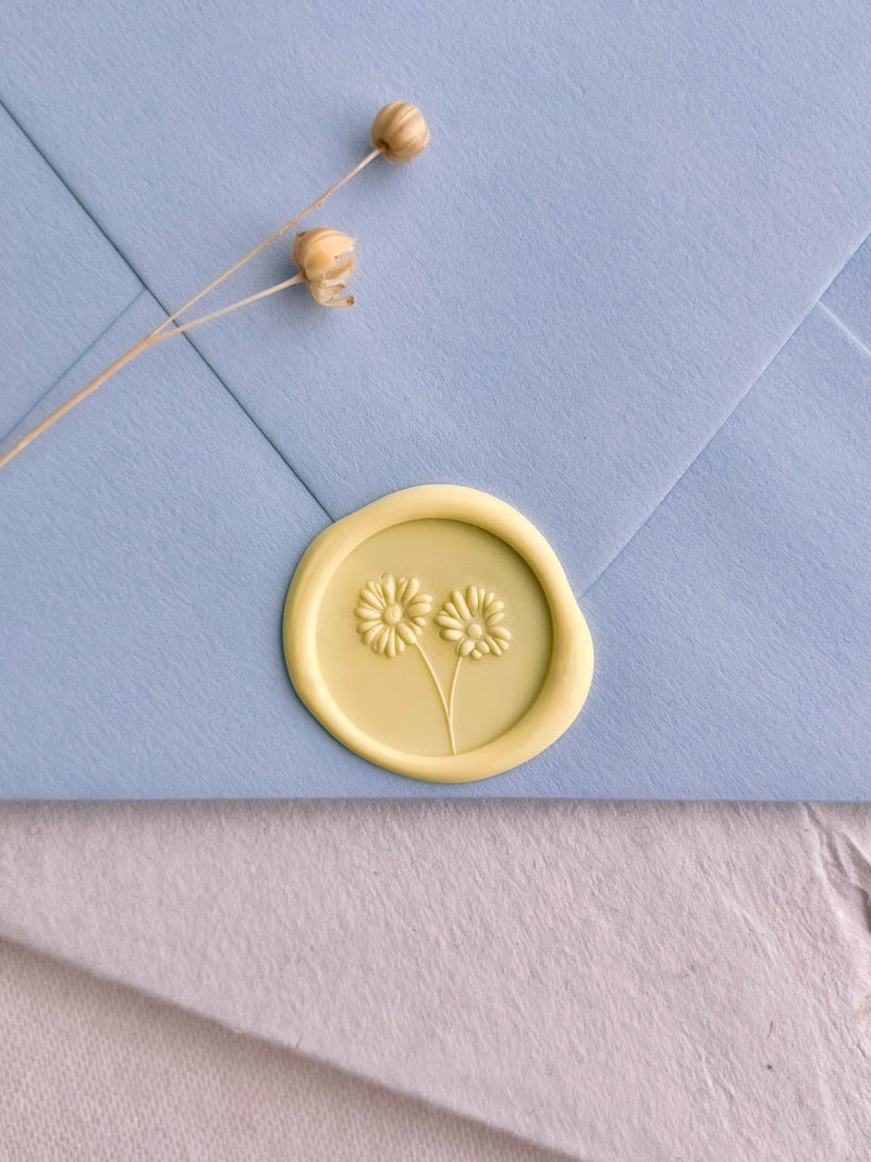 Soft yellow daisy wax seal on a pale blue wedding invitation envelope