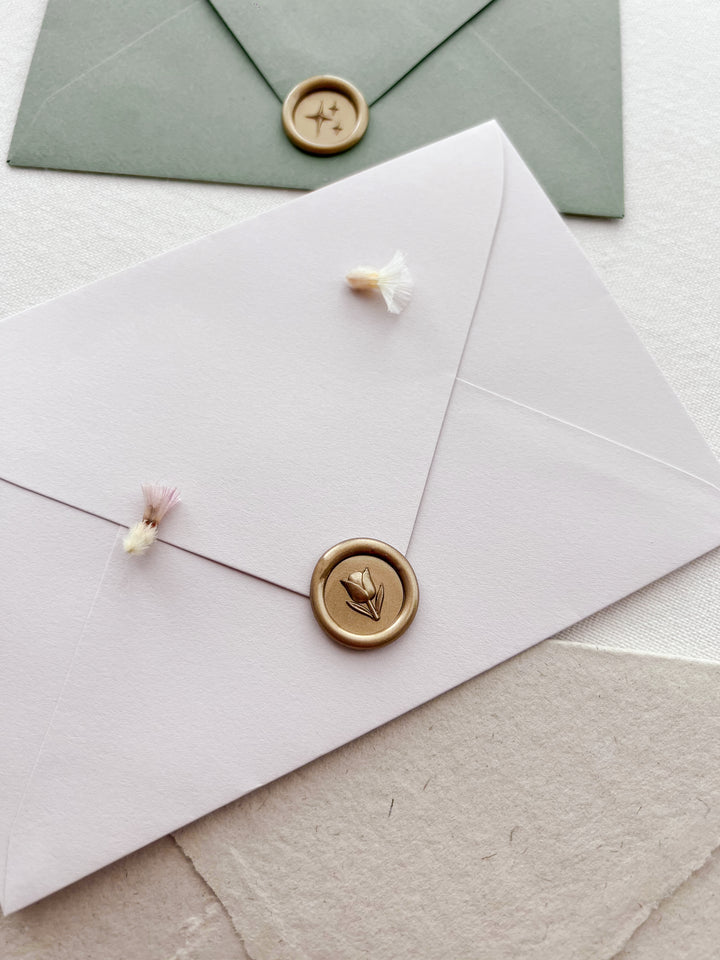 gold 3D mini flower emoji wax seal on a light beige envelope styled with dried florals