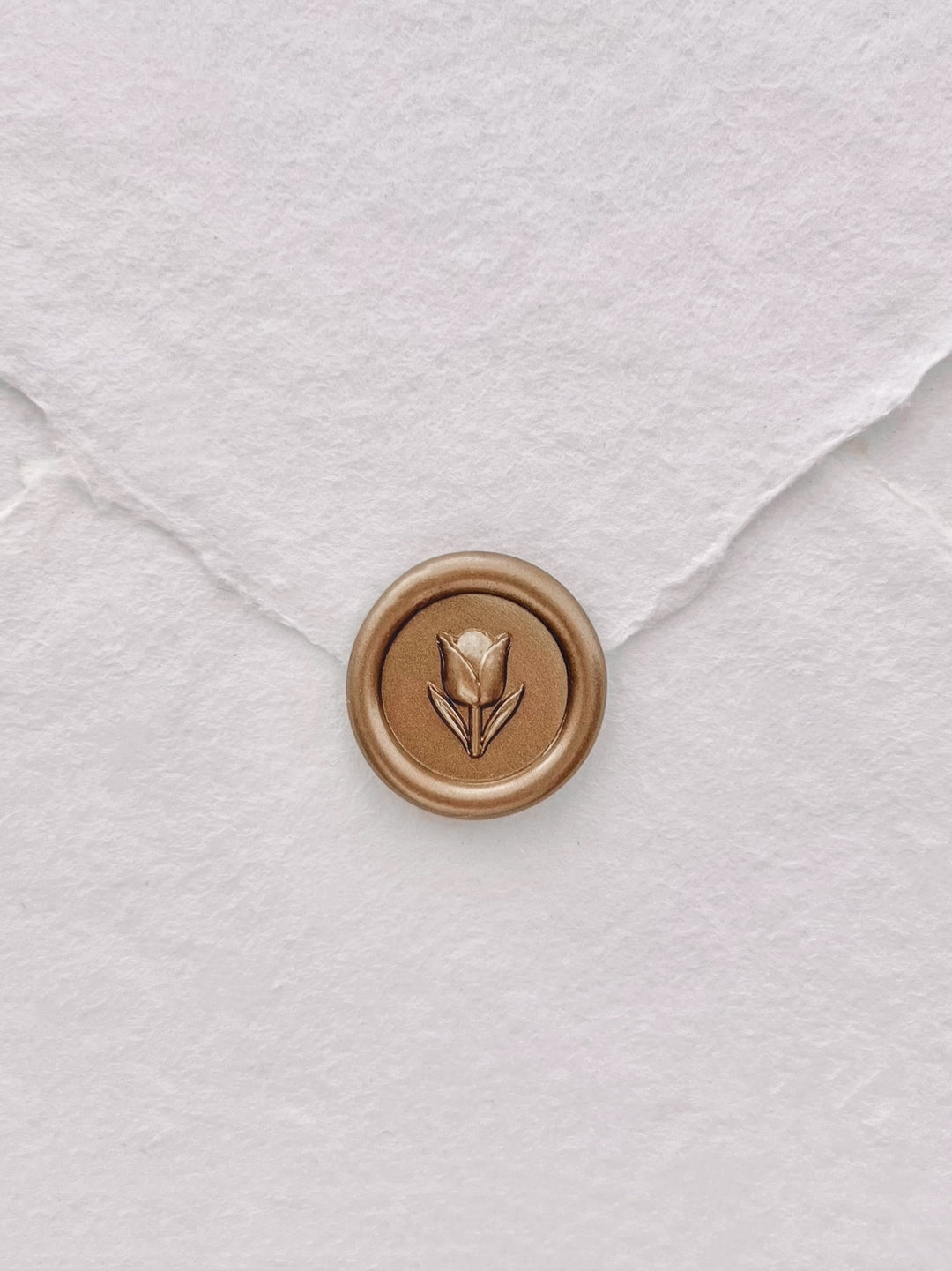 gold 3D mini flower emoji wax seal on a white deckle-edge handmade paper envelope