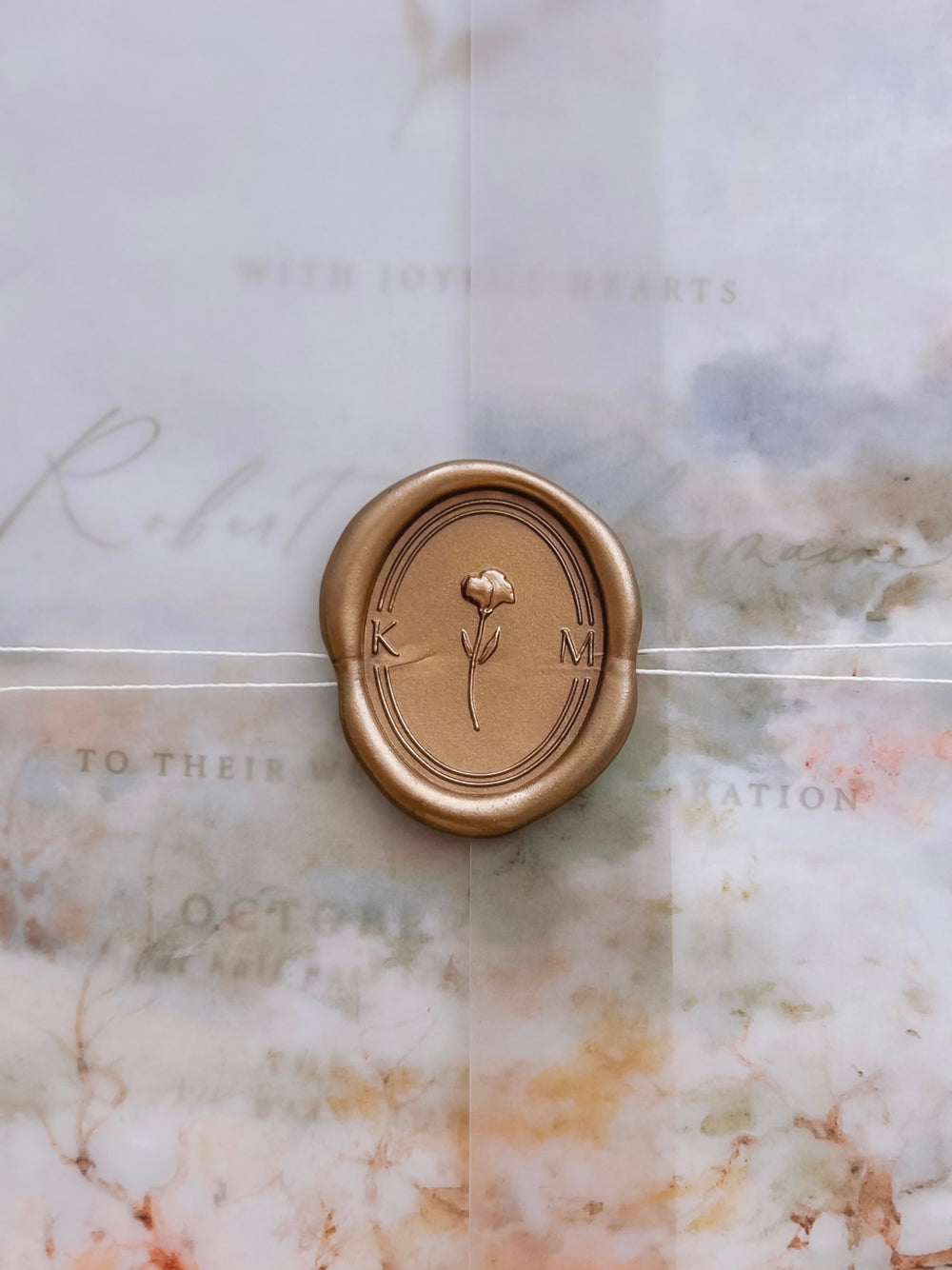 Custom initials floral monogram oval gold wax seal with a 3D floral design in the center with a double border on a wedding invitation vellum jacket