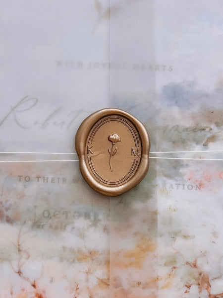 Custom initials floral monogram oval gold wax seal with a 3D floral design in the center with a double border on a wedding invitation vellum jacket