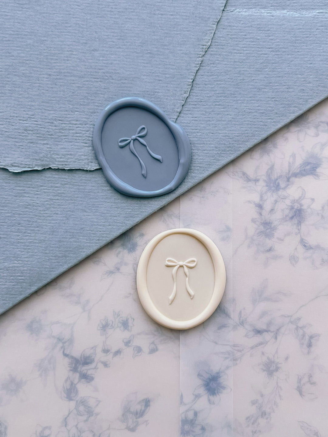 Dusty blue and off-white 3D hand-drawn ribbon bow oval wax seals on a blue envelope and blue floral print vellum jacket