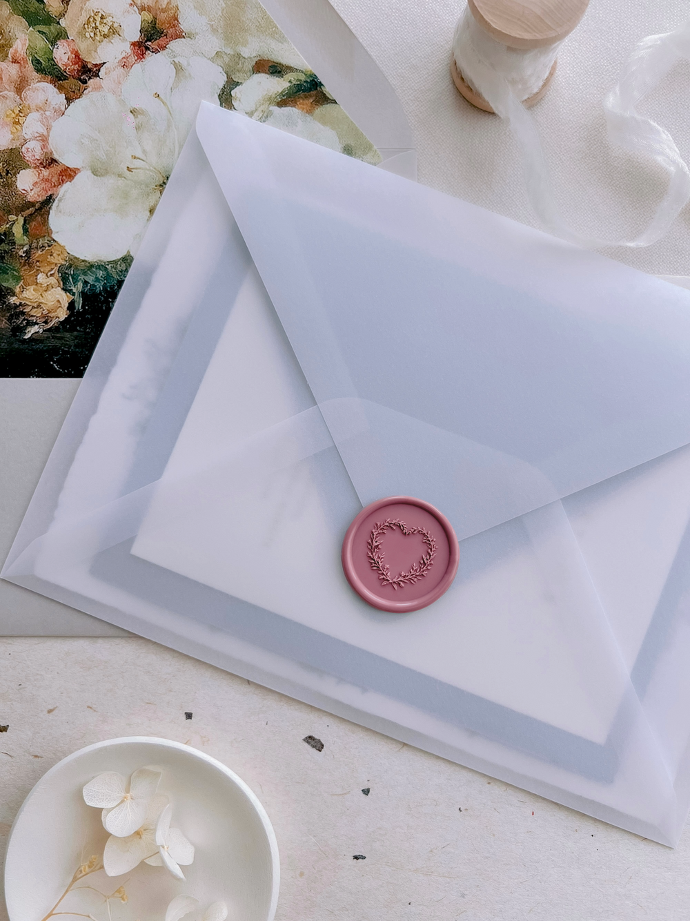 Rose pink heart shaped botanical wreath wax seal on a wedding invitation vellum envelope over a grey envelope with floral envelope liner 