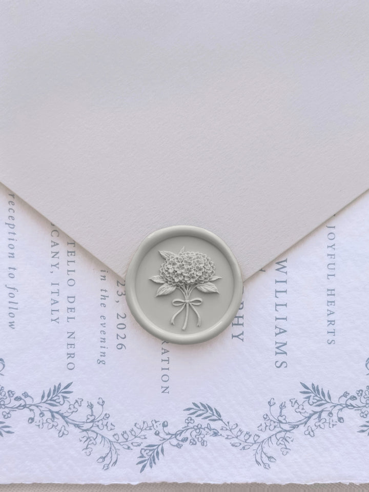 Grey hydrangea flower bouquet wax seal on a beige envelope over a blue botanical wedding invitation card 