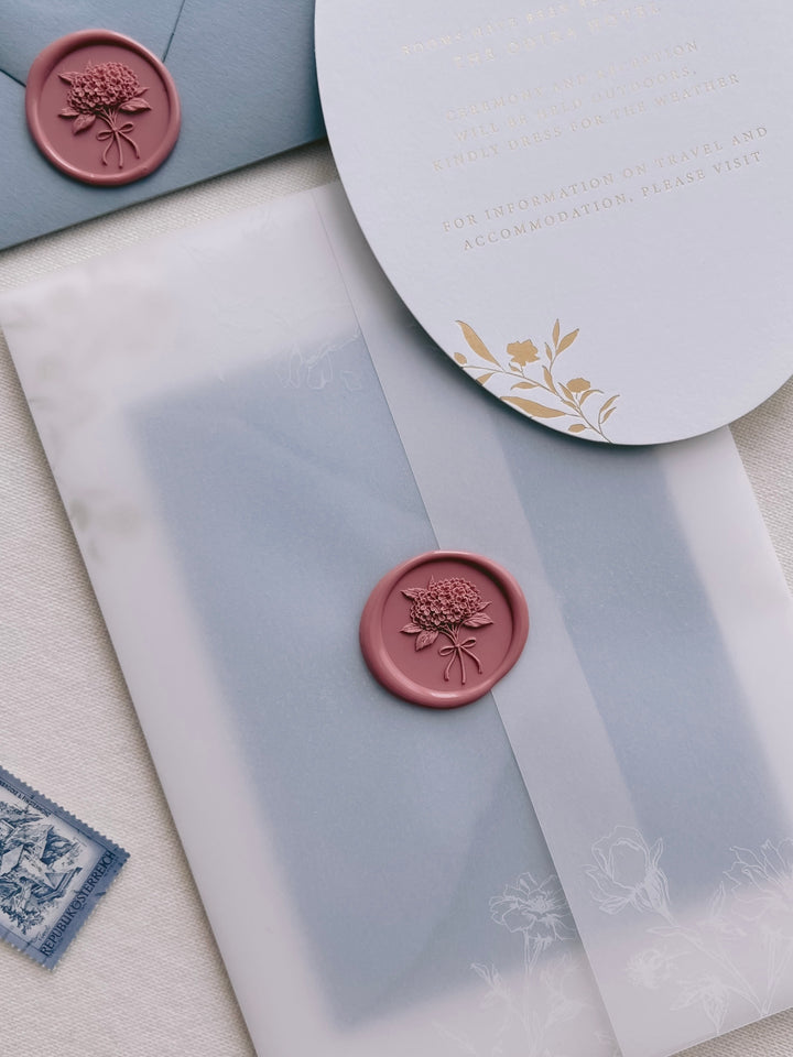 Dusty rose 3D hydrangea bouquet wax seal on a white floral print vellum jacket, dusty blue envelope and a gold foil wedding invitation card