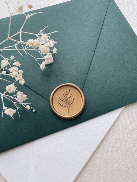 Leaf branch gold wax seal with 3D engraving details on a dark green envelope