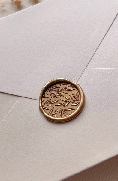 Leaf pattern gold wax seal on a beige envelope